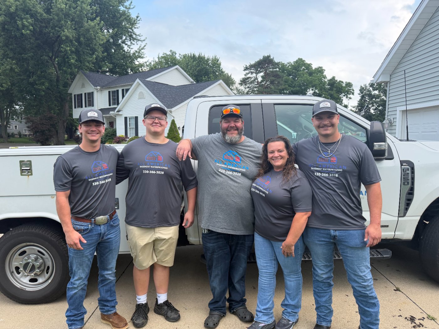 The family team behind All American Basement Waterproofing standing in front of their work truck